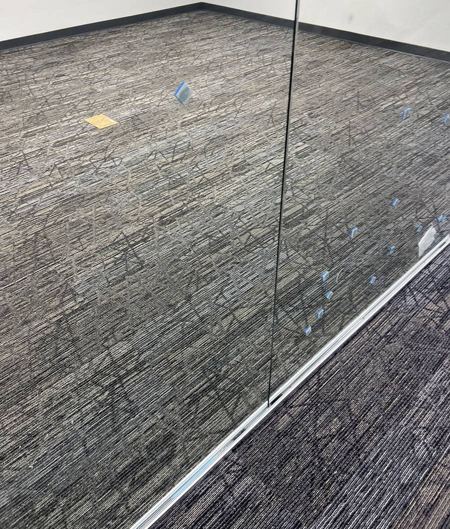 A small office with glass doors in a commercial building with newly installed gray carpeting.