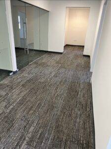 A hallway and small office in a commercial building with new gray carpeting.