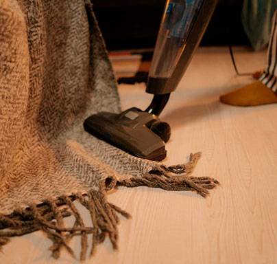 A homeowner vacuuming their hardwood floors as part of a recommended cleaning routine to remove dust and protect wood finish.